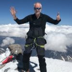 Professor Chris Imray standing on a mountain top celebrating reaching the peak